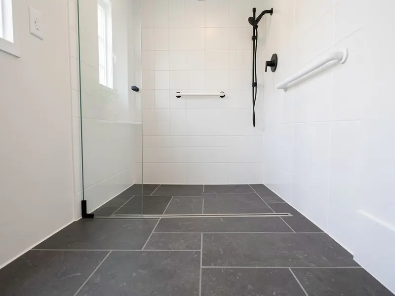 Design rendering of a curbless walk-in shower where the charcoal floor tile runs straight in to a linear drain at the back wall
