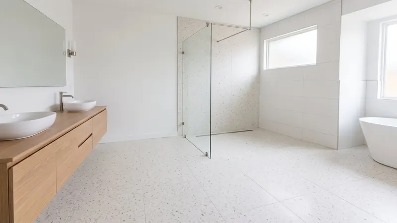 Design rendering of a large primary bathroom with a curbless shower behind a clear glass panel, a linear drain, a terrazzo look floor, a floating white oak double vanity and a freestanding tub