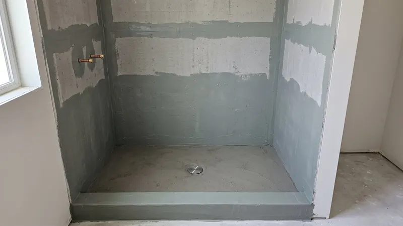 Design rendering of shower walls covered in cement backer board with gray green waterproofing painted over every seam and corner, and a sloped mortar pan below
