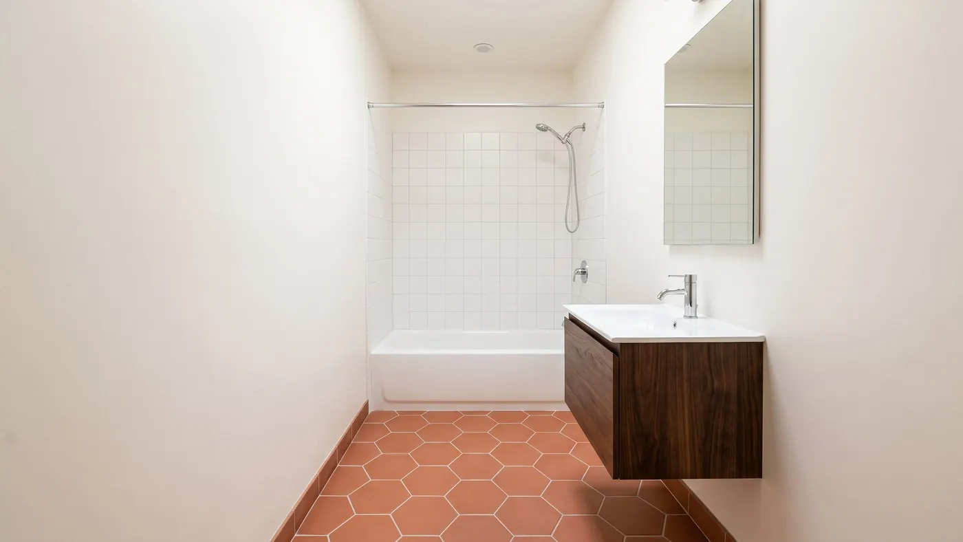 Design rendering of a narrow bathroom with a white tub and square white tile at the far end, a floating walnut vanity with the floor showing beneath it, and terracotta hexagon floor tile